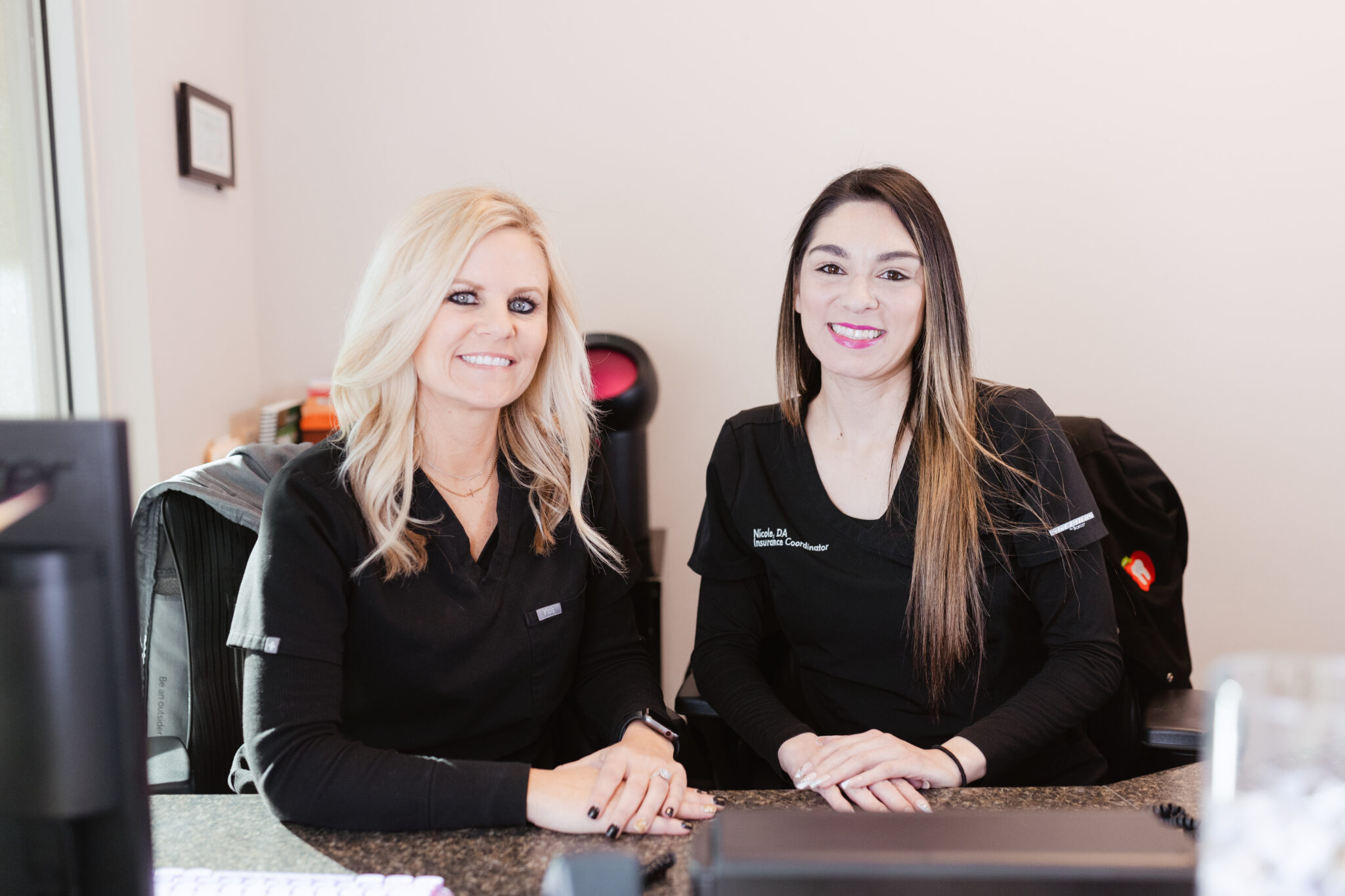 Amber and Nicole, front office team members at Centerpoint Dental in Yucaipa, CA, smiling behind the reception desk in black scrubs