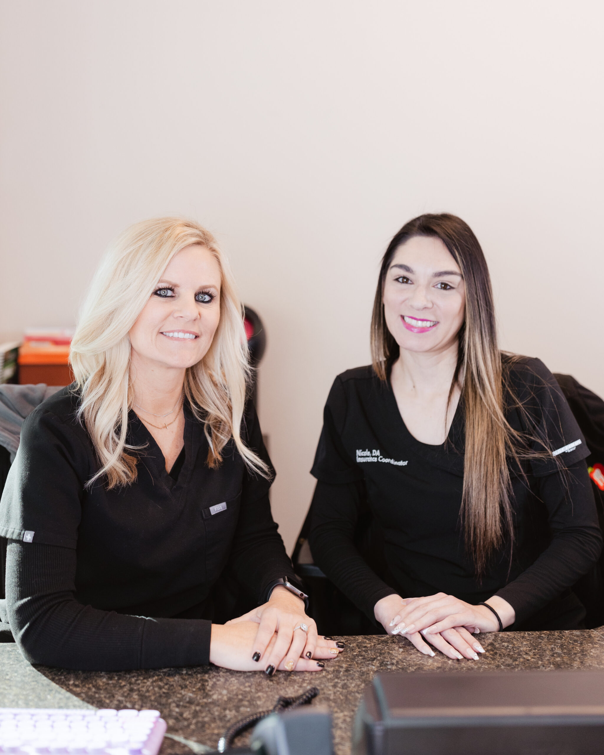 Amber and Nicole, front office team members at Centerpoint Dental in Yucaipa, CA, smiling behind the reception desk in black scrubs