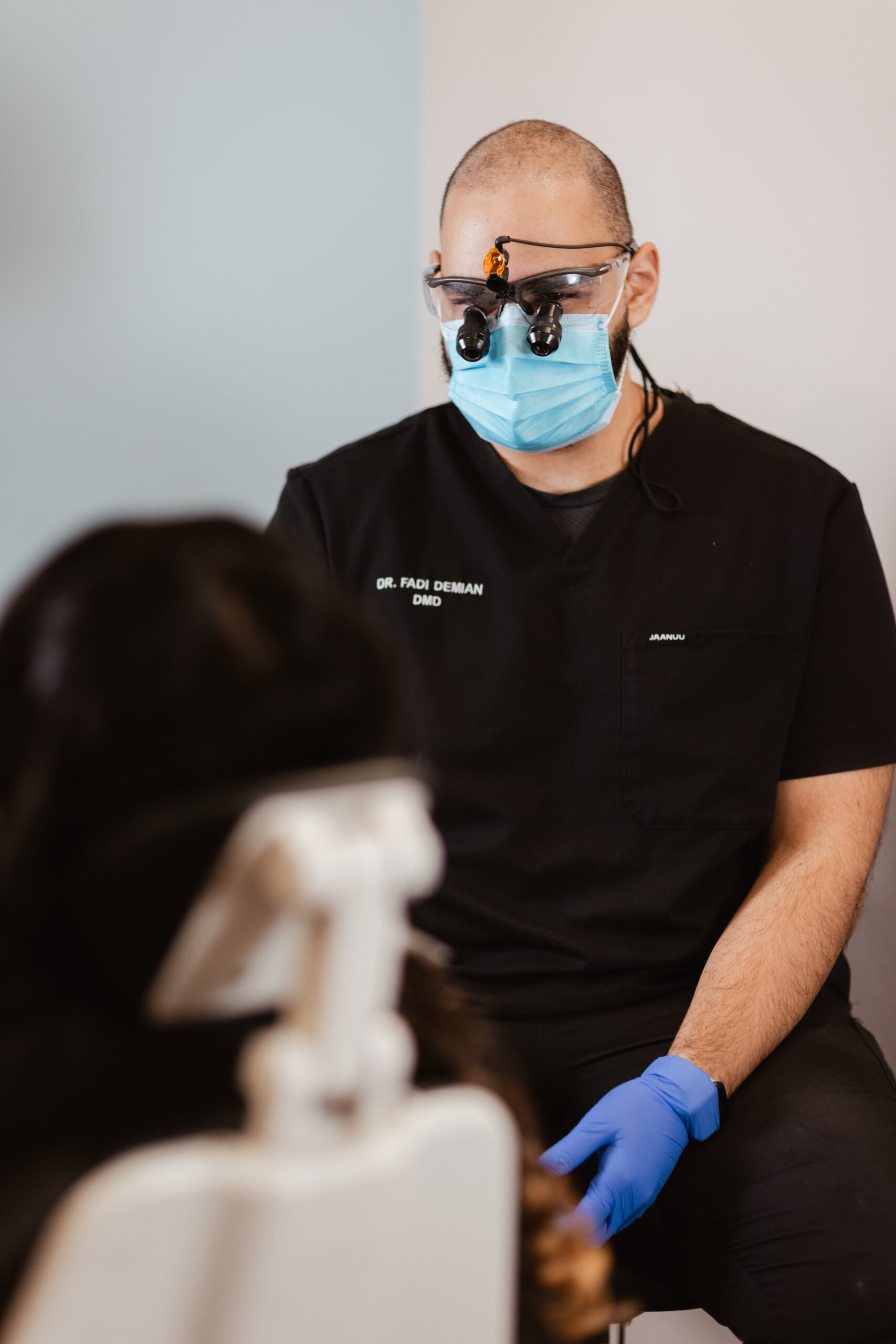 Dr. Fadi Demian, DMD, wearing magnifying loupes and a face mask, sits and attentively consults with a patient during a dental appointment at Centerpoint Dental.